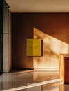 Presentation mockup of a yellow brochure mounted on a warm terracotta wall in a sunlit institutional hallway