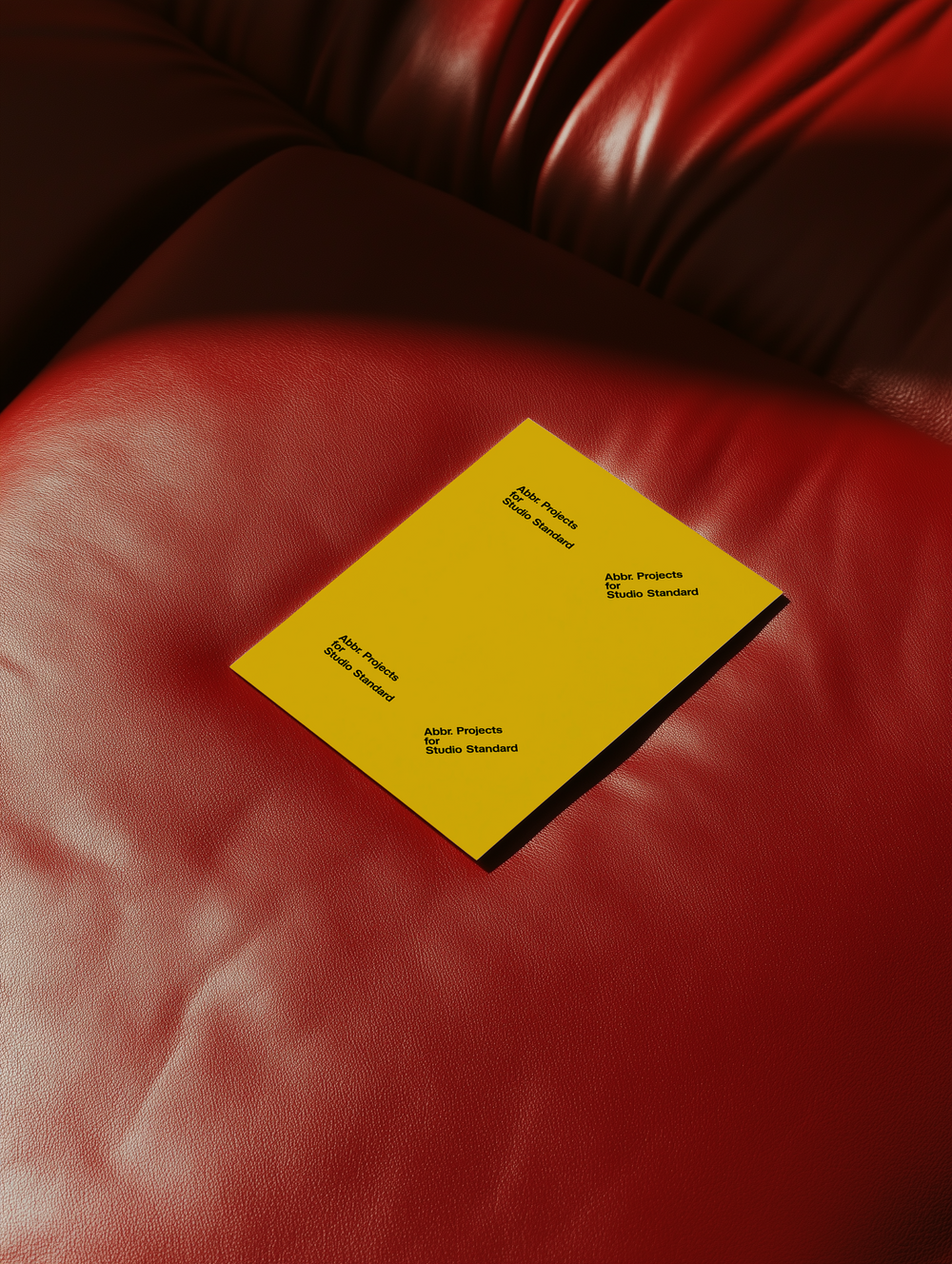 Studio mockup of a yellow brochure placed casually on a red leather sofa by Simon Abranowicz for Studio Standard