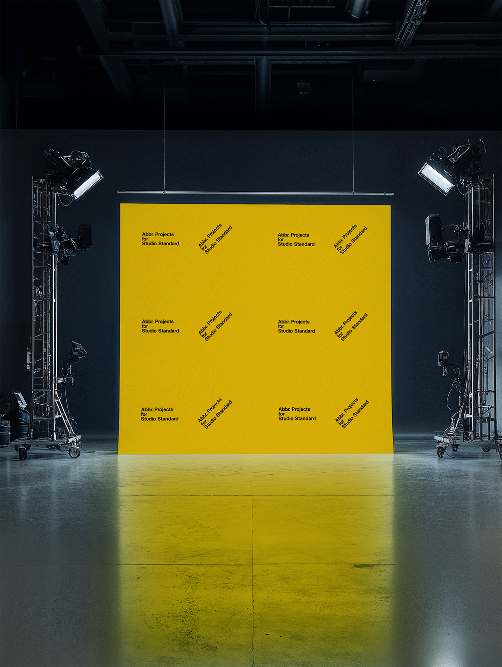 Studio mockup of a yellow step-and-repeat backdrop with professional lighting equipment in a dark photo studio